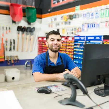 Atendente no balcão de uma loja de materiais de construção, com computador e leitor de código de barras.